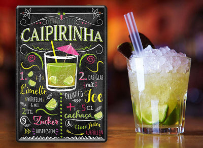 Stilvolles Blechschild mit Cocktail-Rezept für Caipirinha, dekorativ mit Limettenscheiben und Cocktailglas daneben platziert
