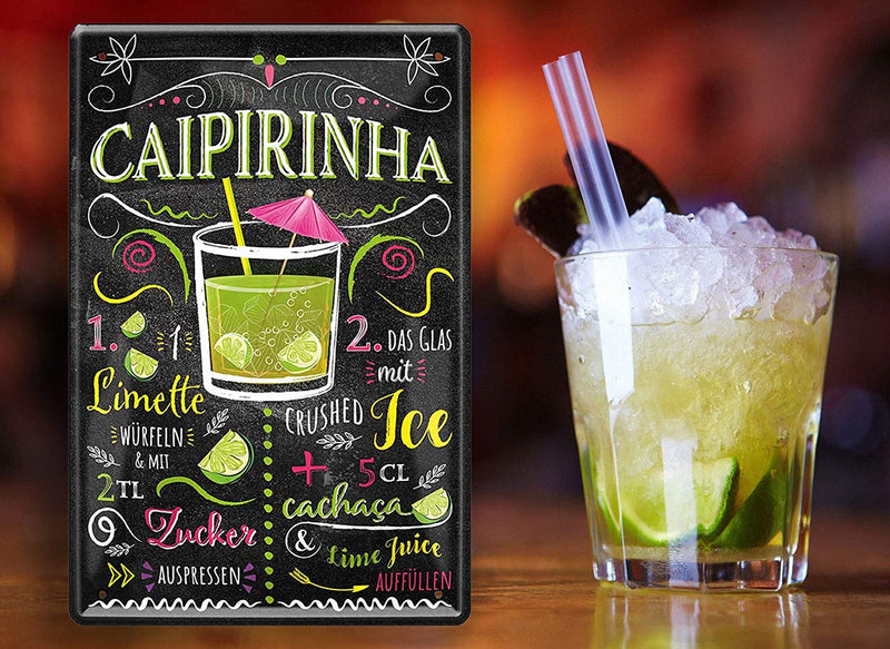 Stilvolles Blechschild mit Cocktail-Rezept für Caipirinha, dekorativ mit Limettenscheiben und Cocktailglas daneben platziert