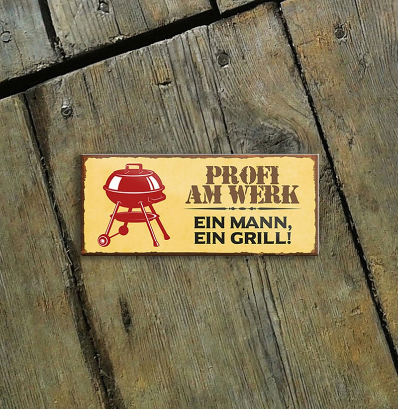 Profi am Werk - Lustiger Grill Spruch auf Dekomagnet. Grill-Symbol und Text "Ein Mann, ein Grill!" auf gelbem Hintergrund. Perfekte Geschenkidee für Grill-Liebhaber vor rustikalem Holzhintergrund.