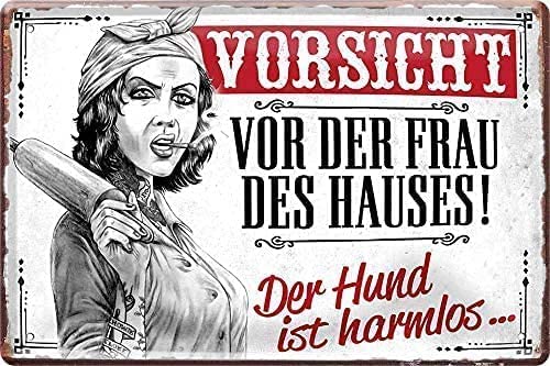 Warnung vor der Herrin des Hauses! Das Blechschild zeigt eine Frau in einer aggressiven Haltung mit einem Kochlöffel in der Hand. Der Text lautet "Vorsicht vor der Frau des Hauses!" und "Der Hund ist harmlos...". Das Bild hat einen rustikalen, vintage-artigen Stil mit einer roten Farbgebung.